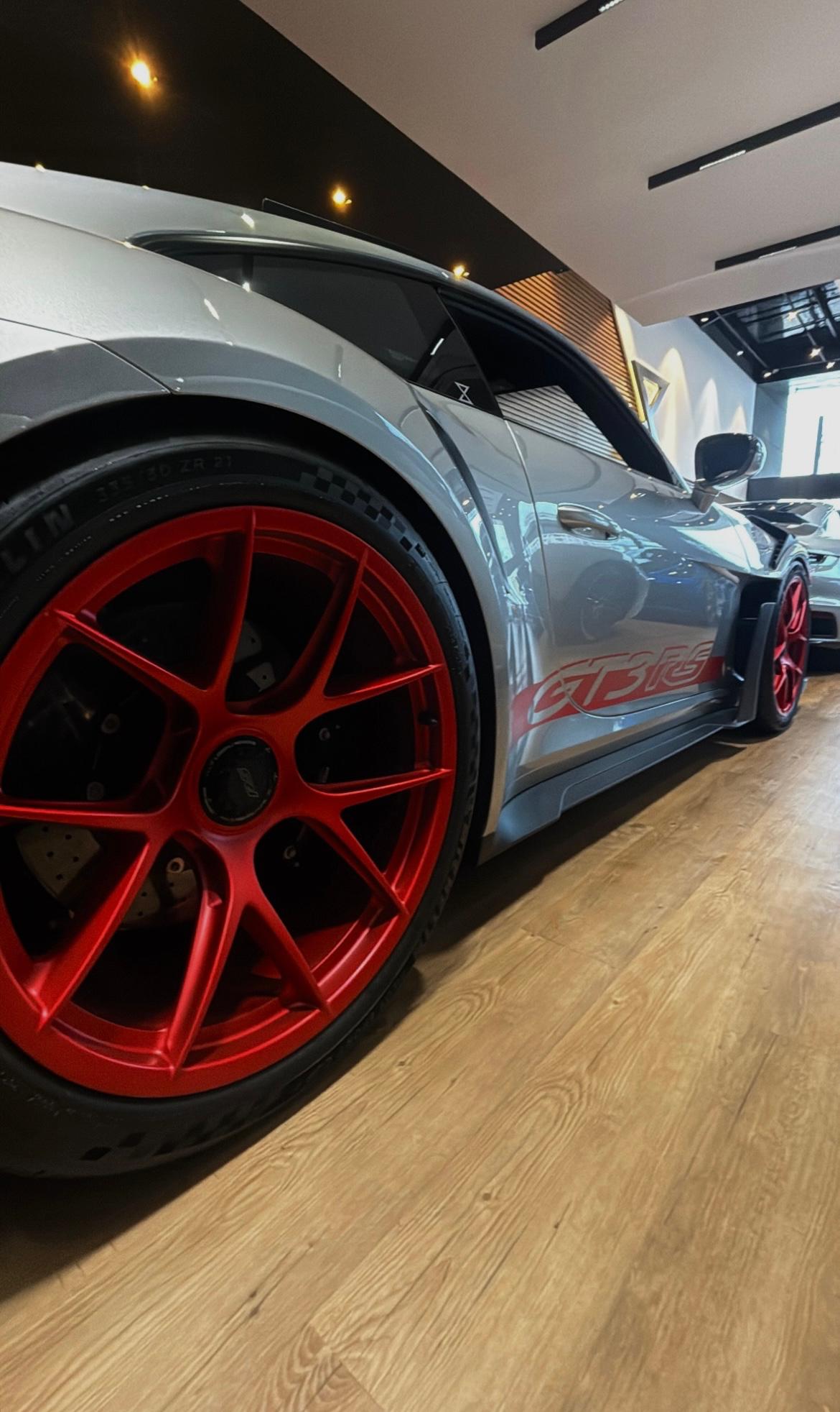 Porsche 911 GT3 RS cinza com rodas vermelhas em showroom