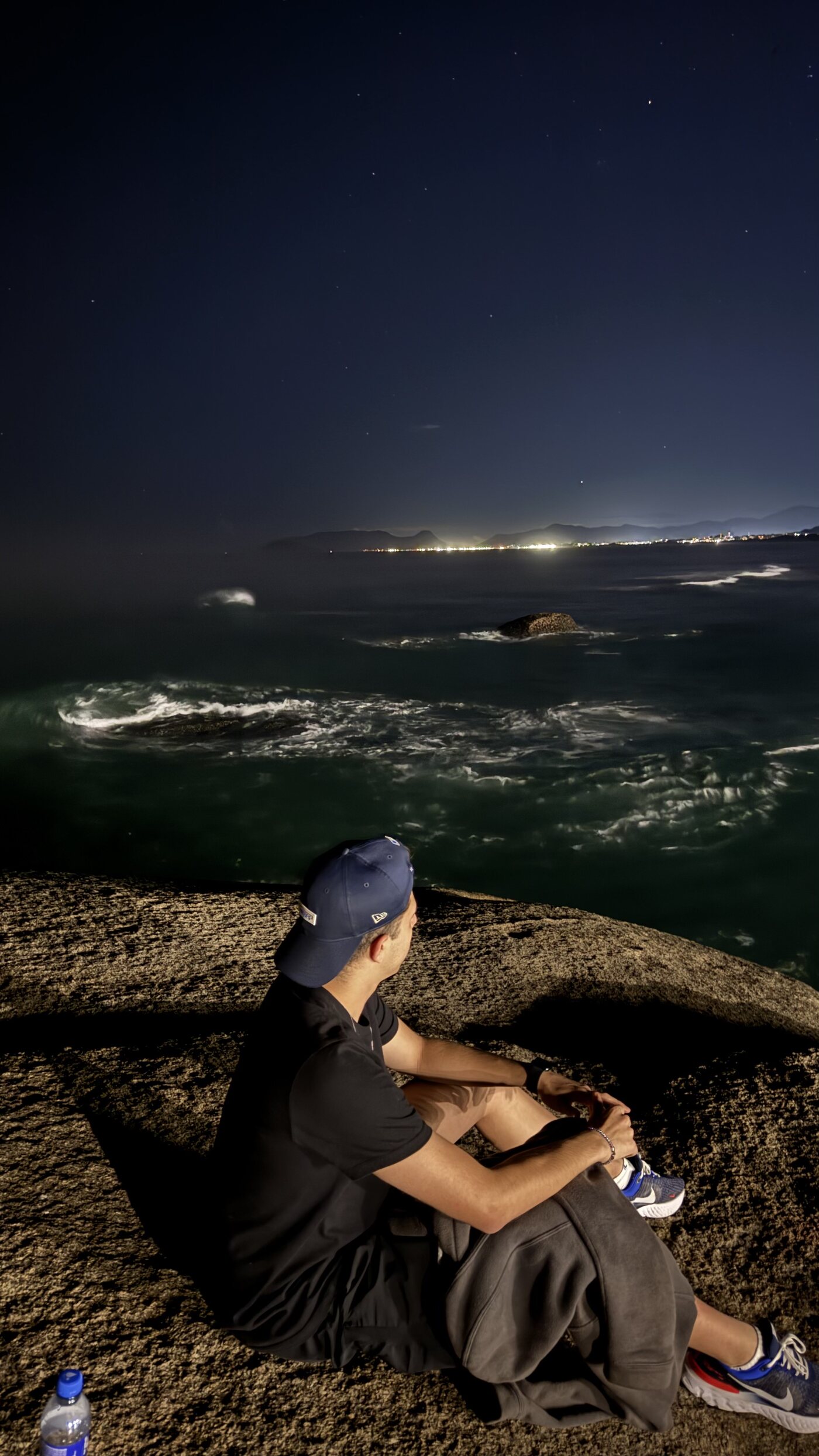 Matheus Barros sentado em uma pedra observando o mar à noite